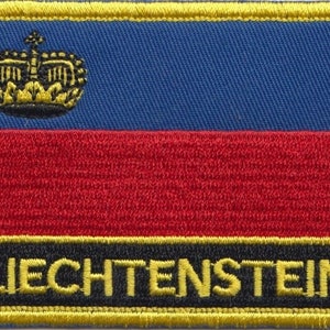 May include: A blue, red and black embroidered patch with a gold crown and the word "LIECHTENSTEIN" in gold lettering.