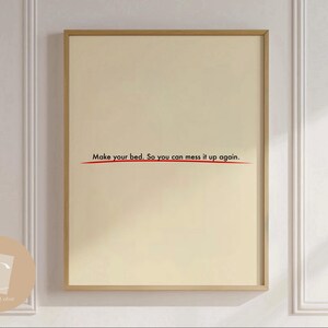 Könnte beinhalten: Ein gerahmter Druck mit beigefarbenem Hintergrund und schwarzem Text, der "Mache dein Bett. Damit du es wieder durcheinander bringen kannst." lautet. Unter dem Text ist eine rote Linie gezogen.