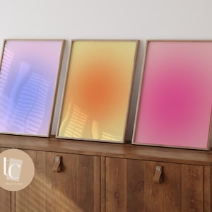 May include: Three framed gradient prints in a light blue, yellow, and pink color scheme. The prints are displayed on a wooden cabinet with a brown finish.