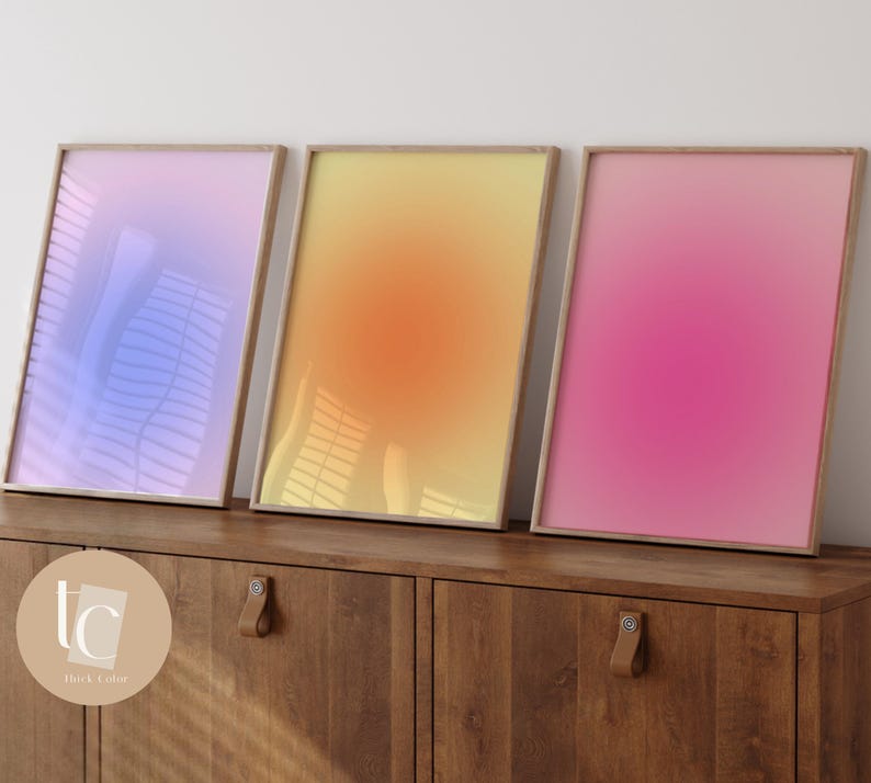 May include: Three framed gradient prints in a light blue, yellow, and pink color scheme. The prints are displayed on a wooden cabinet with a brown finish.
