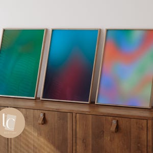 May include: Three framed abstract art prints with a gradient of colors. The prints are in wooden frames and are hanging on a wall above a wooden cabinet.