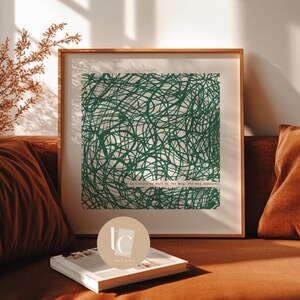 Puede incluir: Una impresión artística enmarcada con un diseño abstracto verde de líneas que se cruzan sobre un fondo blanco. La impresión incluye el texto "as I start to walk in the way, the way appears." La obra de arte se exhibe en un sofá marrón.