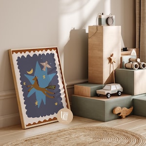 May include: A framed art print featuring a whimsical illustration of a brown horse leaping across a blue star, with a crescent moon and bird. The artwork is in a wooden frame. A toy camera, car, and dinosaur are on display.