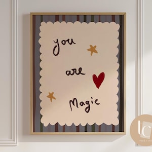 Puede incluir: Una impresión artística enmarcada con un fondo beige y bordes festoneados. Las palabras "you are Magic" están escritas en escritura marrón, con un corazón rojo y estrellas doradas. El marco es de color marrón claro.