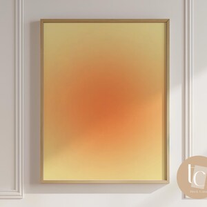 May include: A framed abstract print with a gradient of yellow, orange, and red colors. The print is in a gold frame and is hanging on a white wall.