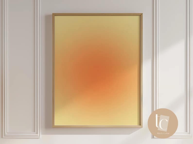May include: A framed abstract print with a gradient of yellow, orange, and red colors. The print is in a gold frame and is hanging on a white wall.