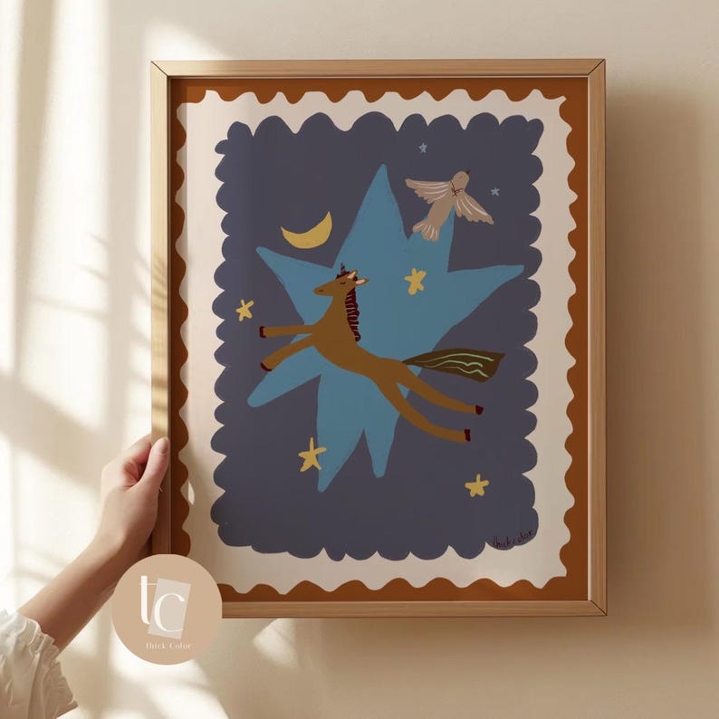 May include: A framed art print featuring a whimsical illustration. A brown horse flies through a blue star against a dark blue background, with a crescent moon, stars, and a small angel. The frame is a light brown color.
