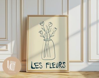May include: A minimalist line art print of a vase with flowers. The vase is a simple, rounded shape and the flowers are stylized with long stems and simple petals. The print is on a light beige background and the text "LES FLEURS" is written in a bold, stylized font.