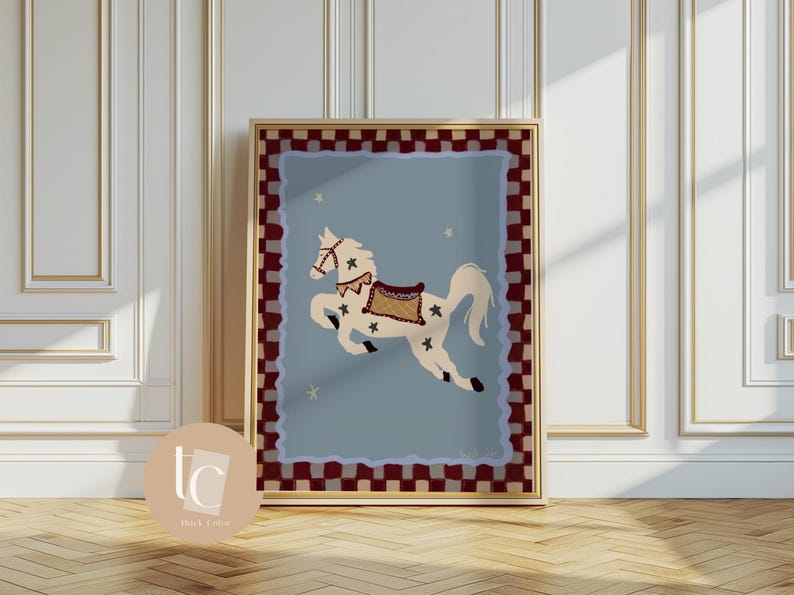 May include: A framed art print featuring a whimsical illustration of a white carousel horse with a brown saddle and star accents, set against a light blue background. The artwork is framed with a gold border and a red and white checkered pattern.