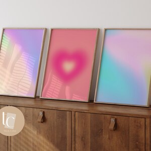 May include: Three framed prints with abstract gradient designs in shades of pink, blue, and purple. The prints are displayed on a wooden shelf.