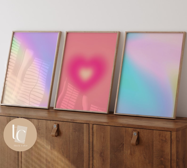 May include: Three framed prints with abstract gradient designs in shades of pink, blue, and purple. The prints are displayed on a wooden shelf.