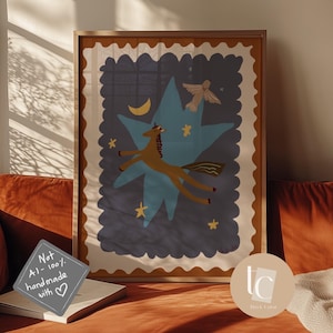May include: A framed art print featuring a whimsical illustration of a brown unicorn soaring through a blue star-shaped design, with a crescent moon and stars. The artwork has a beige border and is displayed on a rust-colored couch.