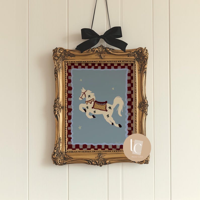 May include: A framed artwork featuring a white horse with star accents on a light blue background. The horse is adorned with a saddle and bridle. The gold frame is ornate, and a black bow suspends the artwork.