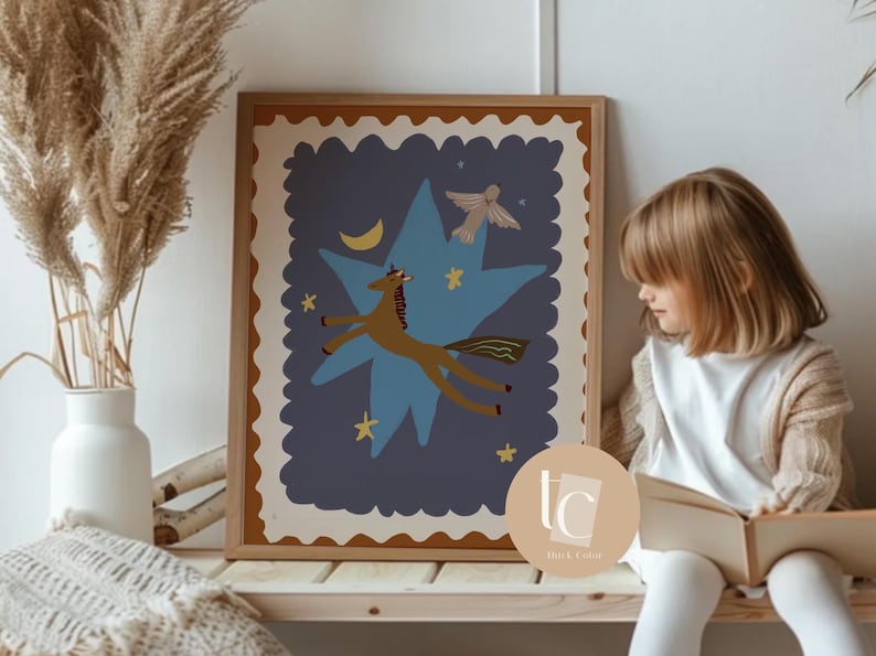 May include: A framed art print featuring a whimsical illustration of a brown unicorn soaring through a blue star-shaped design, with a crescent moon and stars. The artwork has a beige border and is displayed on a wooden shelf.