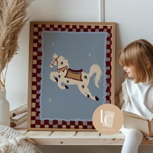 May include: A framed art print featuring a cream-colored carousel horse with a decorative saddle and bridle, set against a light blue background. The frame has a red and white checkered border. Decorative stars are scattered around the horse.