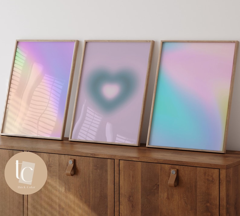 May include: Three framed abstract art prints with a gradient of pink, blue, and green colors. The middle print features a heart shape in the center.