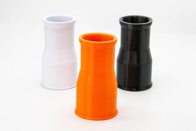 Op de afbeelding: Drie plastic buizen, een witte, een oranje en een zwarte. De buizen zijn allemaal even groot en even gevormd, en ze staan allemaal rechtop op een wit oppervlak.