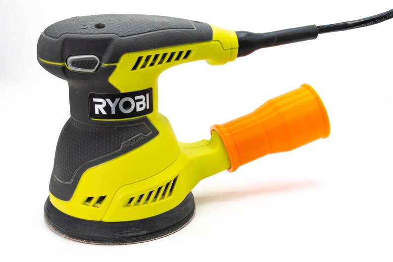 Op de afbeelding: Een gele en zwarte Ryobi elektrische schuurmachine met een oranje stofafzuigbuis. De schuurmachine heeft een zwarte gripzone en een zwart netsnoer.