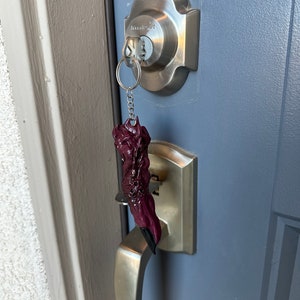 May include: A dark purple, claw-shaped keychain hanging from a silver key. The keychain is attached to a silver key ring and chain. The key is inserted into a silver door lock on a blue door. The door has a silver handle.