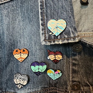 May include: A denim jacket with a variety of heart-shaped pins. The pins feature different designs, including a mummy, a pumpkin, a skeleton, a Frankenstein, and a patchwork heart.