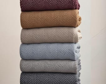 Puede incluir: Una pila de ocho mantas enrolladas en varios colores, incluyendo tonos de rojo, morado, beige, gris y azul. Cada manta presenta un patrón de espiga. Las mantas están cuidadosamente apiladas, mostrando su textura y variaciones de color.