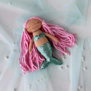 May include: A handmade mermaid doll with pink yarn hair, a green sequined tail, and a pink and white seashell bikini top.