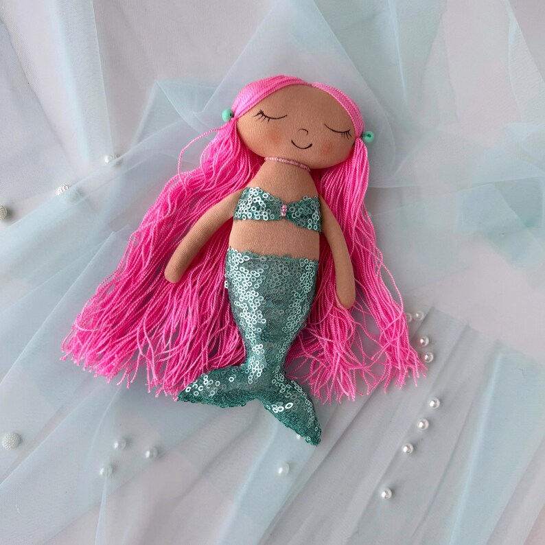 May include: A handmade mermaid doll with pink yarn hair, a teal sequin tail, and a pink and white seashell bikini top.