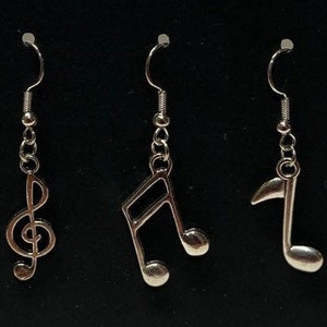 May include: Six pairs of silver earrings with music note and treble clef charms. The earrings are on a black background.