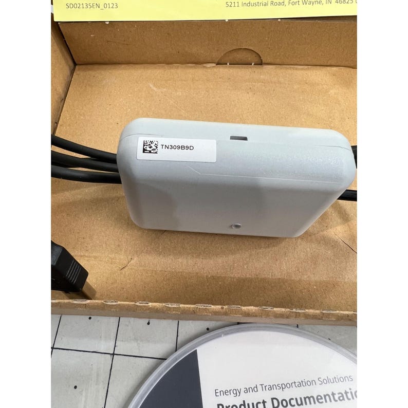 May include: A light gray electronic device with the text "TN309B9D" on a white label. The device has black cables and a USB connector. The device is in a cardboard box with a product documentation disc.