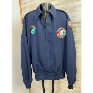 May include: Navy blue zip-up jacket with a collar, featuring patches including an American flag and a circular emblem with an eagle and the text "Cold War Veteran". The jacket has a ribbed hem and cuffs.