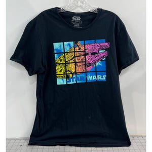 Puede incluir: Camiseta negra con un gráfico colorido de una nave espacial de Star Wars dentro de una cuadrícula. El diseño incluye tonos amarillos, naranjas, rosas y azules, con las palabras "STAR WARS" en la parte inferior. Cuello redondo y mangas cortas.