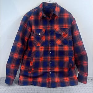 May include: A red, blue, and brown plaid jacket with two chest pockets and two side pockets. The jacket has a button-up front and a collar. The jacket is hanging on a hanger.