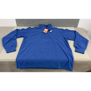 May include: A long-sleeved, royal blue fleece pullover with a mock neck collar. The shirt has a small tag attached near the collar. The sleeves have ribbed cuffs. The garment is laid flat on a neutral surface.