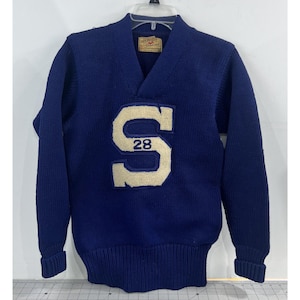 Könnte beinhalten: Ein marineblauer Vintage-Wollpullover mit einem cremefarbenen "S" und der Nummer "28" auf der Vorderseite. Der Pullover hat einen V-Ausschnitt und gerippte Bündchen und Saum. Ein klassisches Sportbekleidungsstück.