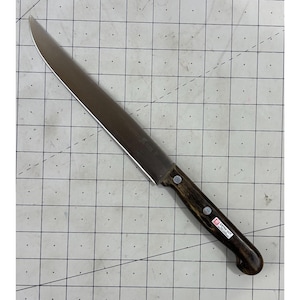 May include: A stainless steel carving knife with a dark wooden handle. The blade is long and curved, and the handle is riveted with two silver rivets. The knife has a label that says "EXTRA CUT".