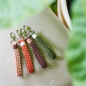 May include: Four colorful keychains made of braided rope with silver key rings. The keychains are in shades of brown, orange, and green.