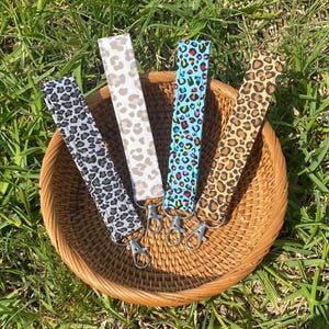 May include: Four keychains with different animal print patterns. The keychains are made of fabric and have silver key rings. The keychains are displayed on a woven basket.