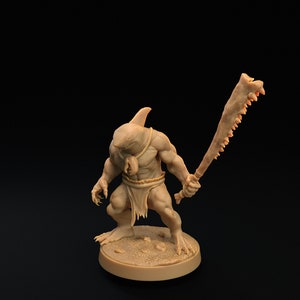 May include: A miniature figurine of a humanoid creature with a shark head, holding a jagged bone weapon. The figure is painted in a light brown color and stands on a round base.