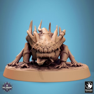 May include: A tan-coloured fantasy creature figurine with sharp teeth and horns, posed on a circular base. The figurine has a menacing expression and is set against a blue background. The text "Fate Unbound" is visible on the base.