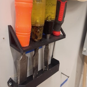 Könnte beinhalten: Ein schwarzer, an der Wand befestigter Werkzeughalter mit Meißeln und Schraubendrehern. Die Schraubendreher haben gelbe und schwarze Griffe, und die Meißel haben Metallklingen. Der orangefarbene Meißel befindet sich links. Die Werkzeuge sind ordentlich angeordnet.