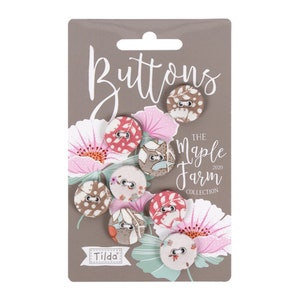 Könnte beinhalten: Eine Packung dekorativer Stoffknöpfe aus der Tilda Maple Farm Collection. Die runden Knöpfe haben verschiedene Blumen- und Musterdesigns in Rosa-, Braun- und Cremetönen. Auf der Karte steht das Wort "Buttons".