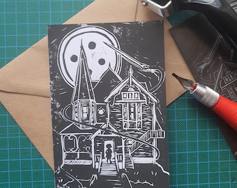 May include: Black and white linocut print of a spooky house with a large moon and a small figure standing in the doorway. The house has a pointed roof and many windows. The moon has a button-like design.