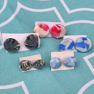 May include: A set of 10 colourful, round, marbled earrings. The earrings are made of polymer clay and have a variety of colours, including black, white, red, blue, and grey.