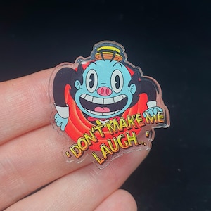 May include: A clear acrylic pin featuring a cartoon character with a blue face, black hair, and a top hat. The character has a wide grin and is surrounded by a red swirl design. The text "DON'T MAKE ME LAUGH..." is displayed.