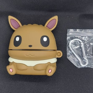 May include: A brown and beige silicone phone case featuring a cartoon image of a Pokemon character. The case has a small loop for attaching a keychain.