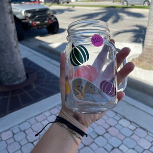 May include: A clear glass mason jar with a handle, decorated with colorful fall-themed stickers. The jar has a price tag that reads "$10".