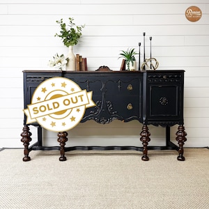 May include: A black painted vintage buffet with ornate details and carved legs. The buffet has two drawers and a cabinet door. The buffet is sold out.