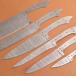 Peut inclure: Ensemble de six lames de couteau en acier Damas non finies. Les lames sont de tailles et de formes différentes, avec une finition à motifs distinctive.