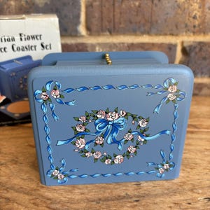 May include: A blue and white floral design coaster set with a ribbon and roses. The set is in a box that says "Victorian Flower Lace Coaster Set".