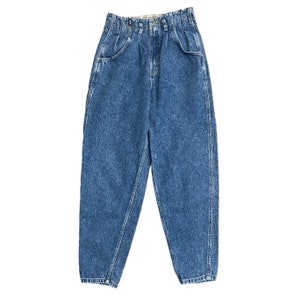 Puede incluir: Un par de pantalones vaqueros azules de mezclilla con cintura alta y corte holgado. Los vaqueros tienen un lavado claro y un aspecto descolorido.